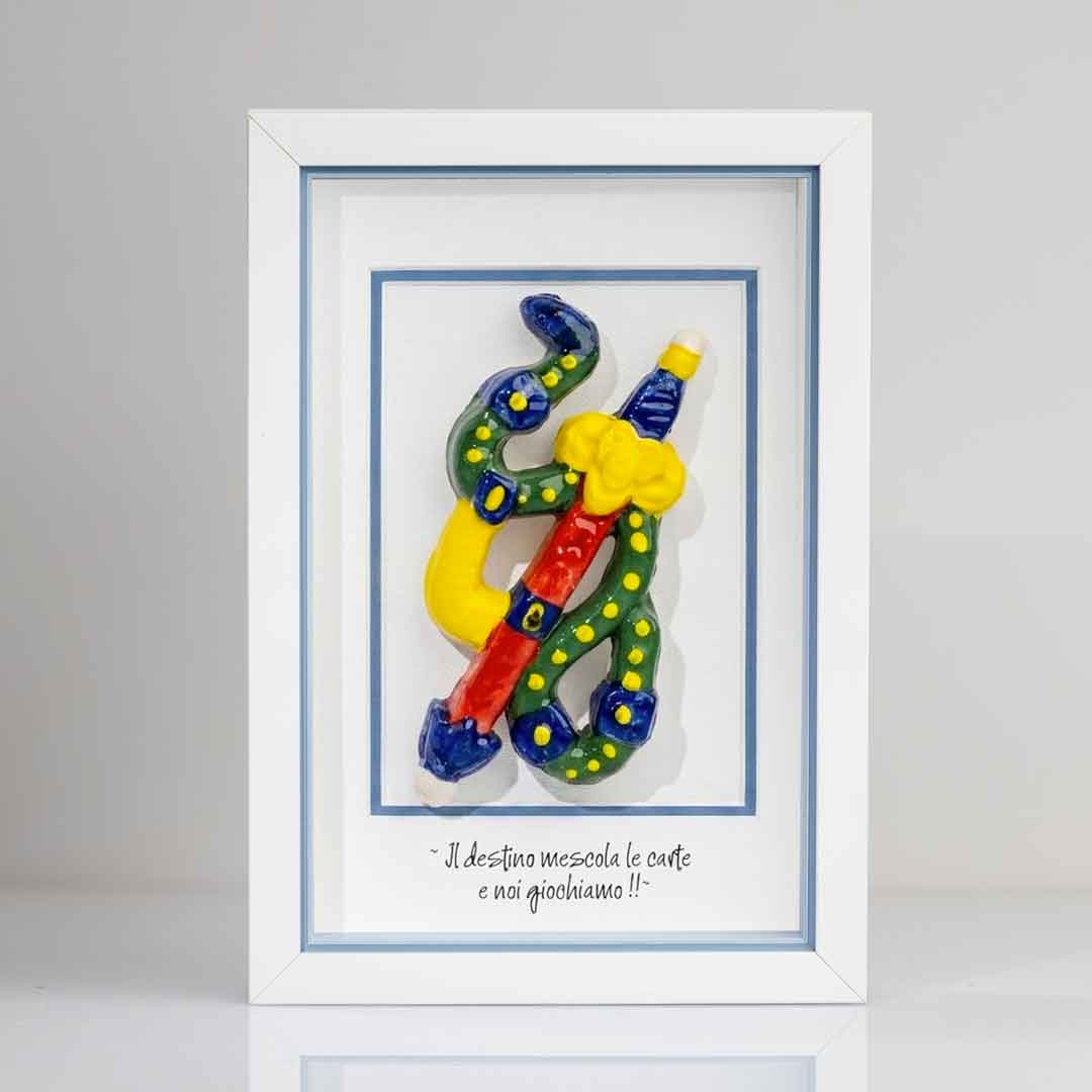 Quadro con cornice contenente una riproduzione tridimensionale in ceramica dell'Asso di Spade delle carte napoletane. Raffigura una spada con impugnatura gialla e azzurra, avvolta da un elemento sinuoso verde a pois gialli. In basso è presente la scritta in corsivo: "Il destino mescola le carte e noi giochiamo!!". Il bordo interno della cornice è azzurro